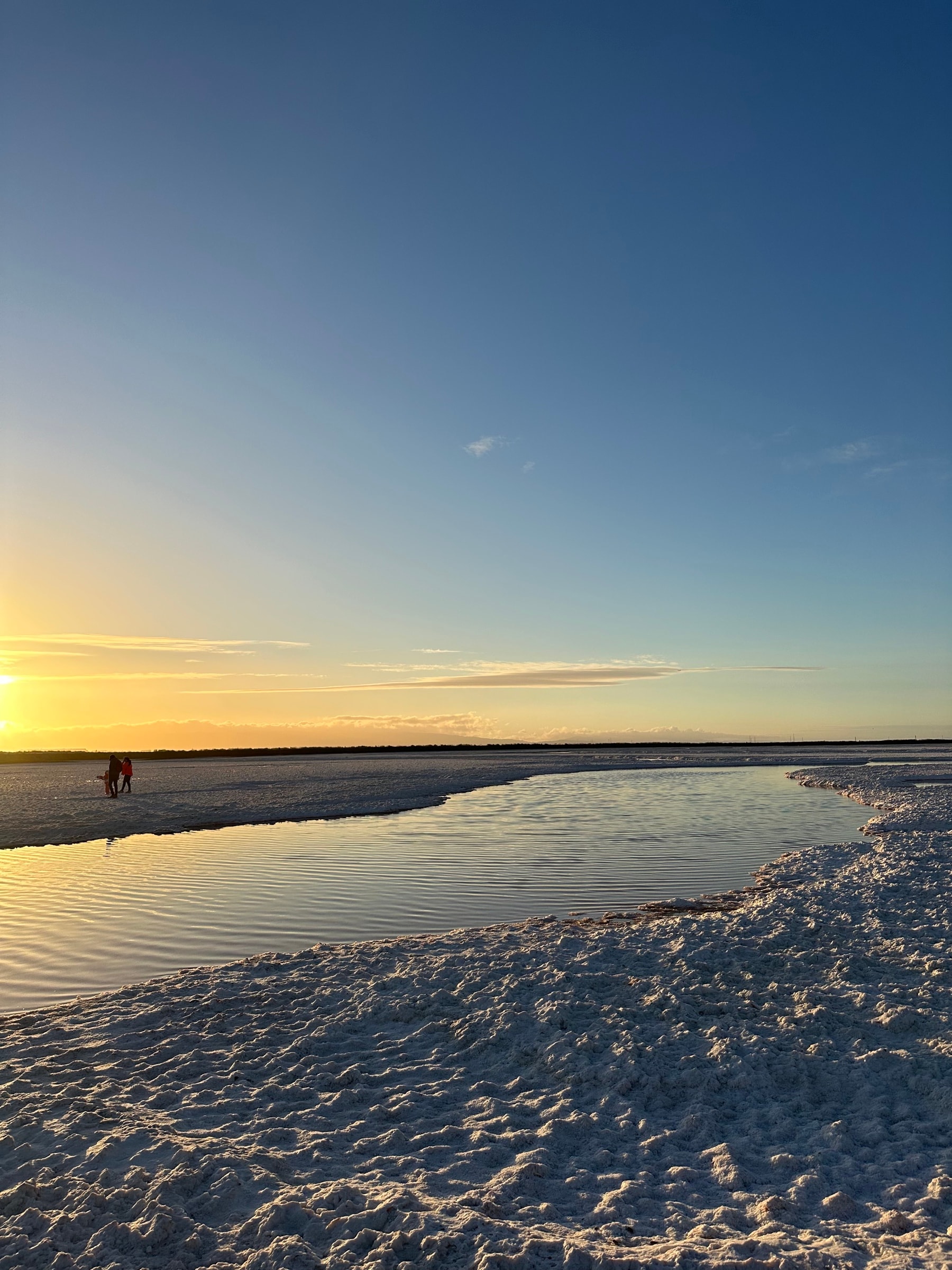 A tide pool meeting the shore at sunset, with a figure walking along the water's edge